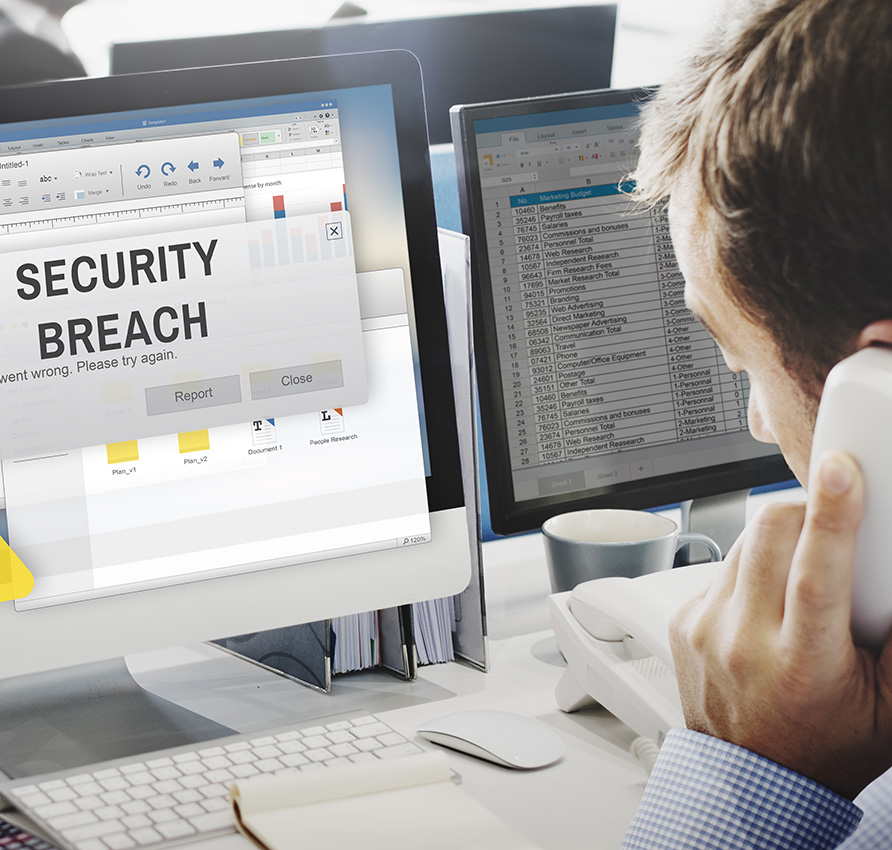 Man on the phon looking at a security breach alert on his computer