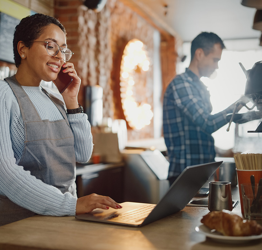 Couple working at a small coffee shop, handling the phone and the coffee maker